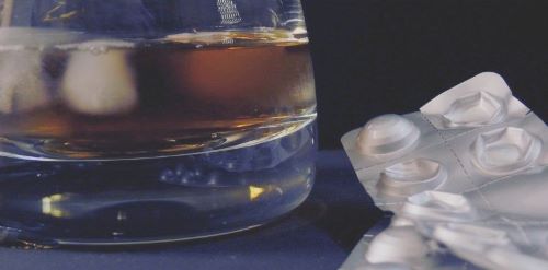 Glass of alcohol on table with medication next to it